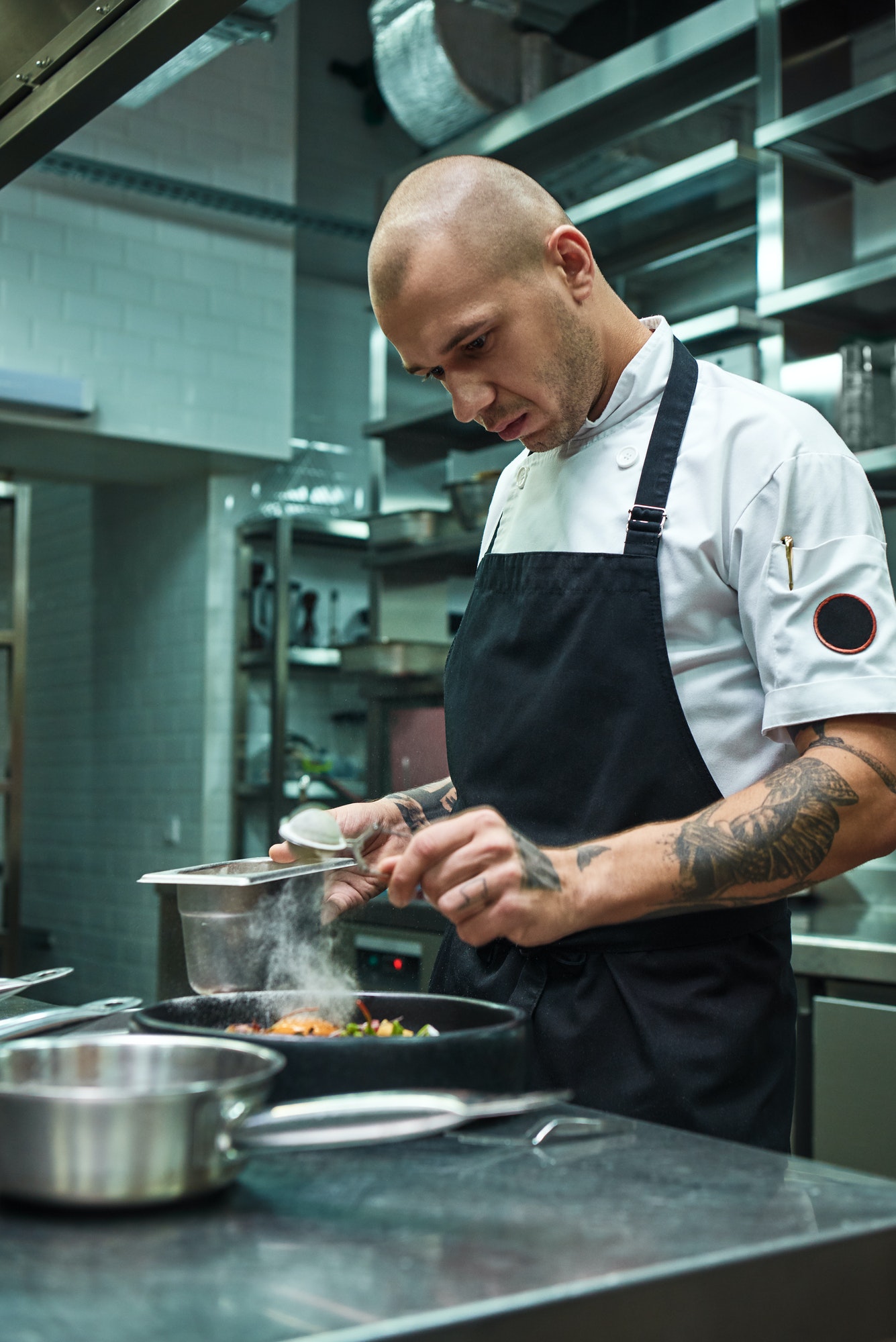 Need more spices. Vertical photo of restaurant chef with several tattoos adding a special spice to