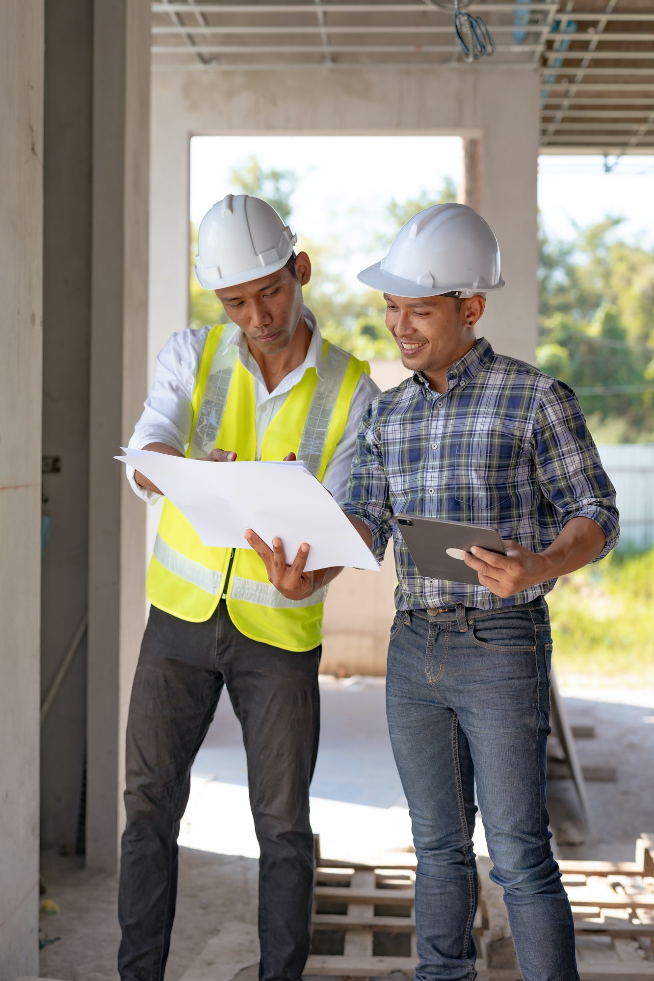 Two Asian male engineers are inspecting a job site and looking at drawings, consulting and debugging