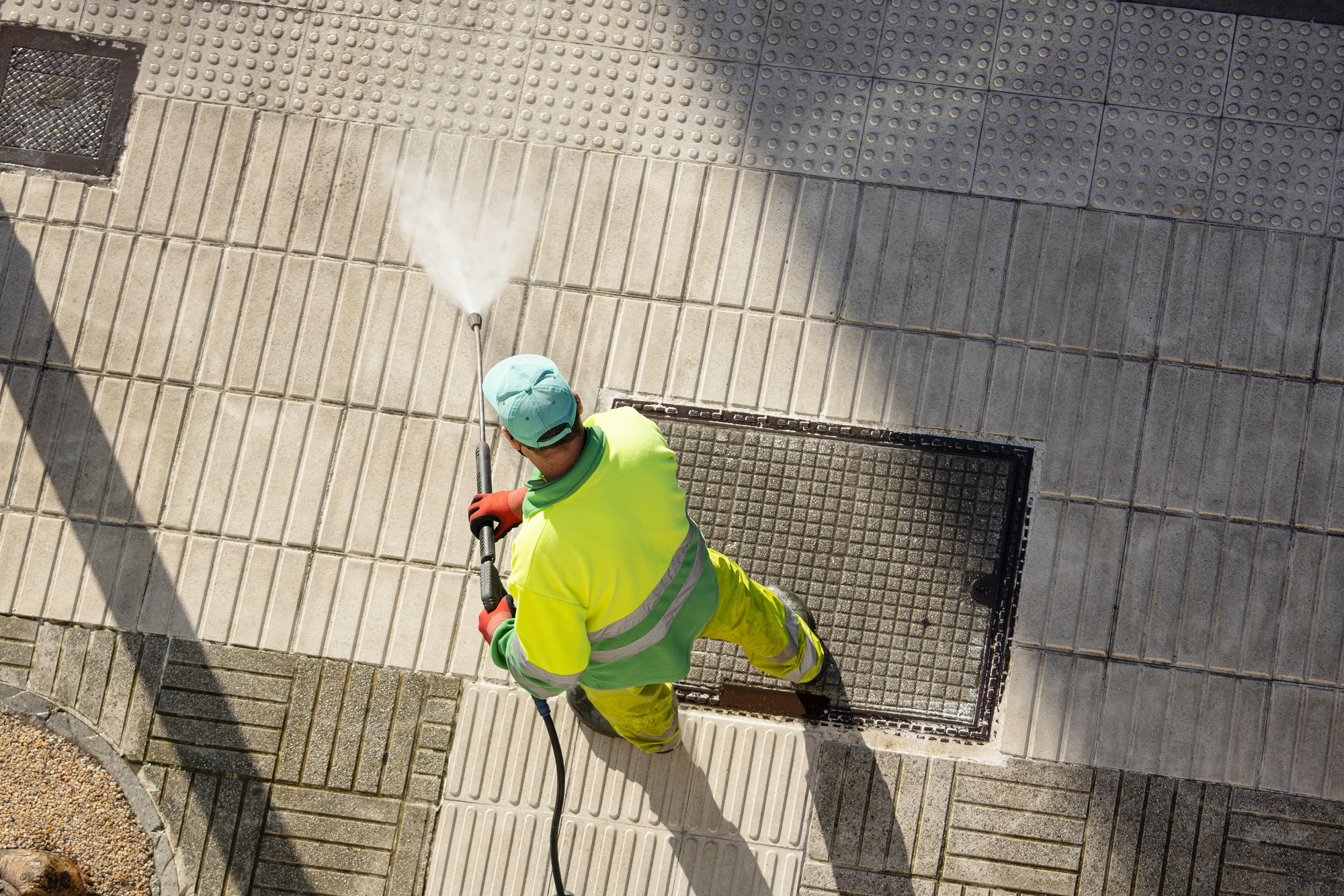 Worker cleaning a street sidewalk with high pressure water jet machine