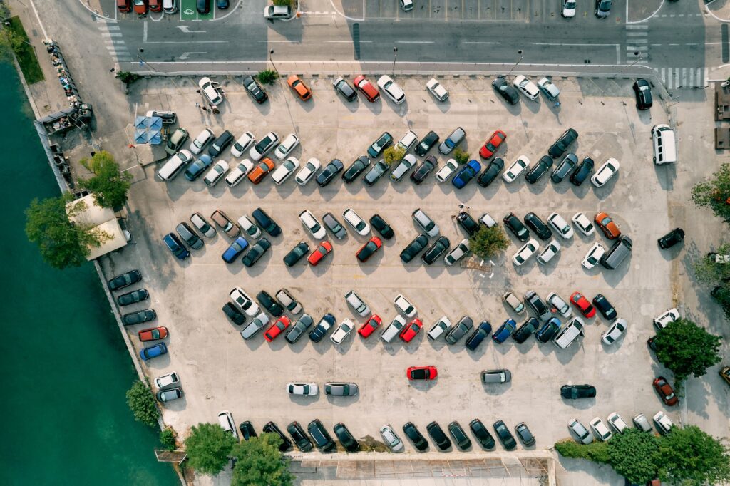 Large parking lot with colorful cars standing in rows on the seashore. Drone